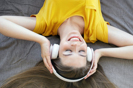 Smiling young lady in headphones listening to music or audio book on her bed, overhead viewの写真素材