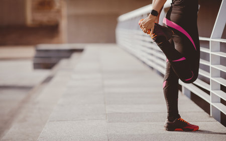 Morning exercise outside. Modern african american girl in sportswear doing workout for leg at stadiumの写真素材