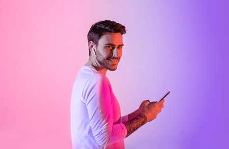 Young man smiling while using smartphone against colorful backdrop