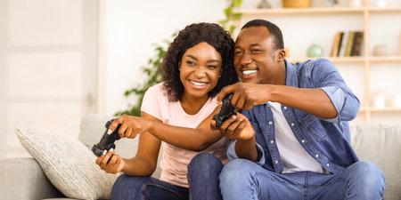 Joyful african american couple with joysticks at homeの写真素材
