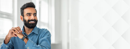 Confident smiling bearded indian man posing at office, looking aside at copy space, sitting at workplace, panoramaの写真素材