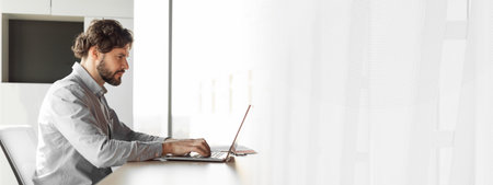 Side view of handsome mature businessman working at office, using laptop computer, sitting at desk, copy spaceの写真素材