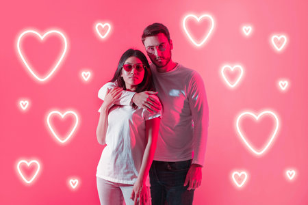 Couple poses playfully against a vibrant pink heart-themed backdropの写真素材