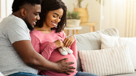 Happy pregnant couple putting future baby little boots on tummyの写真素材