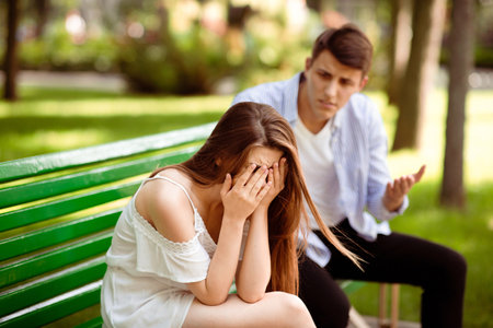 Sad young girl crying during conflict with her boyfriend on bench at park