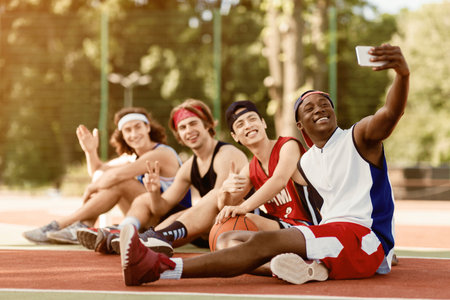 Group of happy basketball players taking selfie while resting after game at outdoor arena, free spaceの写真素材