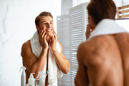 Confident young man looking in the mirror, touching faceの写真素材