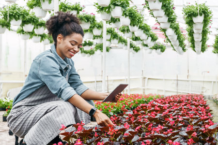 Smiling african american girl works in greenhouse with digital tablet and flowersの写真素材