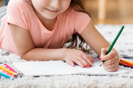 Girl Drawing Picture Using Colorful Pencils Lying On Floor Indoors