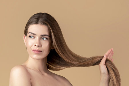 Lovely young girl in bath towel holding her long silky hair on beige backgroundの写真素材