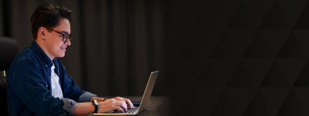 Side view of positive young guy typing on laptop keyboardの写真素材