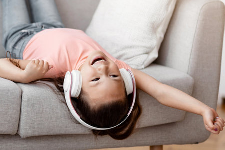 Girl Listening Music Having Fun Sitting Upside-Down On Sofa Indoorsの写真素材