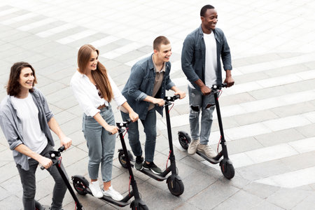Four friends having ride on electric kick scooters