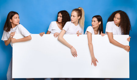 Girls Pulling Apart White Board Standing Over Blue Backgroundの写真素材