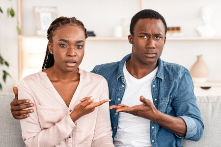 Relationship Misunderstanding. Confused Black Couple Sitting On Couch At Family Counselors Officeの写真素材