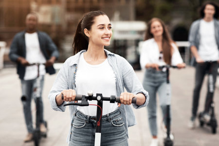 Teenagers riding scooters on a sunny urban street in a diverse setting
