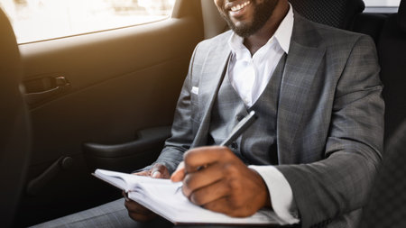Happy black businessman sitting in car, taking notes