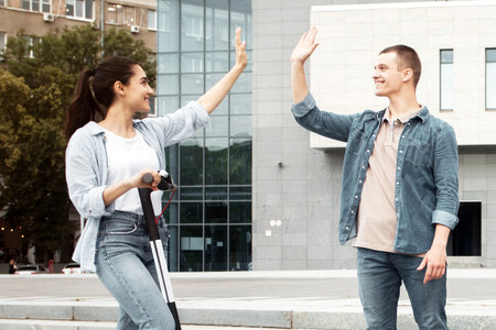 Diverse teenagers riding scooters and greeting each other in urban settingの写真素材
