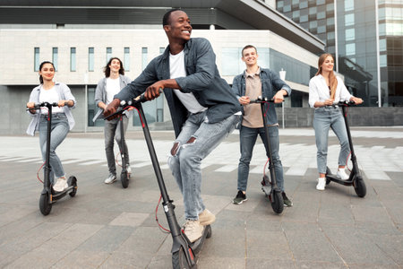 Five excited friends having ride on motorized kick scootersの写真素材