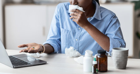Sick Black Female Office Worker Taking Antivirus Pills On Workplaceの写真素材