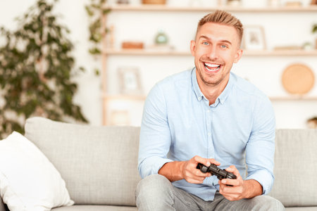 Excited emotional guy sitting on sofa playing video games