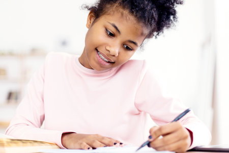 African Teen Girl Doing Homework Writing In Exercise-Book At Homeの写真素材