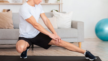 Stretching and workout in morning during covid-19. Muscular guy in sportswear works out at homeの写真素材