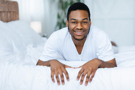 Positive African Man Lying In Bed Smiling To Camera Indoorsの写真素材