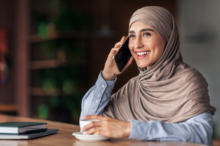 Cheerful arab lady talking on phone while resting at cafeの写真素材