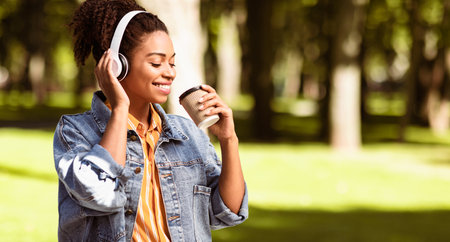 African Millennial Girl With Headphones Having Coffee Walking Outside, Panoramaの写真素材
