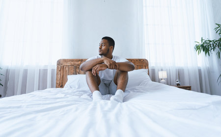 Thoughtful African American Man Looking Aside Sitting In Bedroom Indoorsの写真素材