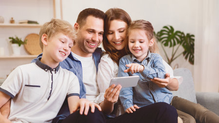 Family Of Four Using Smartphone Sitting On Couch At Homeの写真素材