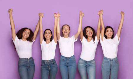 Cheerful Multiethnic Ladies Holding Hands Posing Together Over Purple Backgroundの写真素材