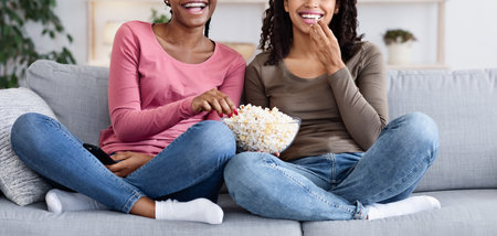 Two black girls having fun at home, watching comedyの写真素材