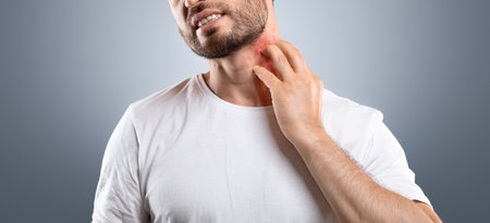 Bearded man scratching neck on grey background, having annoying itch