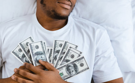 African Man Sleeping Holding Money Lying In Bed At Homeの写真素材