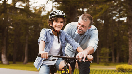 Boy learning to ride bicycle with his happy dadの写真素材