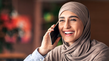 Laughing muslim girl talking on phone while resting at cafeの写真素材