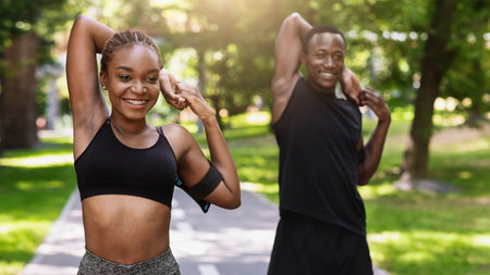 Sporty african couple exercising before jogging at park, stretching arm muscles outdoors