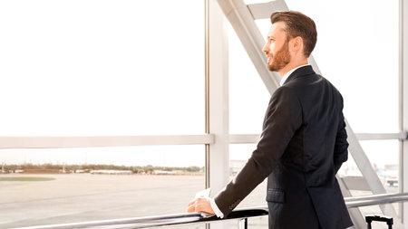 Side view of businessman standing next to window at airportの写真素材