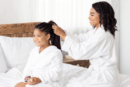 Home Beauty Salon. Loving Black Mom Braiding Hair To Her Little Daughter