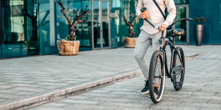 Young man enjoying a coffee while standing next to his bike on the streetの写真素材