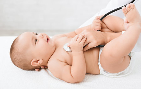 Doctor examining little baby with stethoscope in clinic.