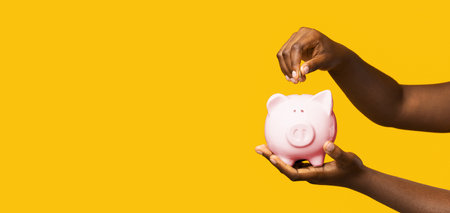 Money Savings. Unrecognizable black woman putting coin into piggybank over yellow backgroundの写真素材