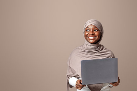 Online Career. Dreamy Smiling Black Muslim Woman In Hijab Holding Laptop Computer