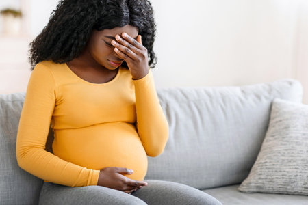Black pregnant woman suffering from headache at homeの写真素材
