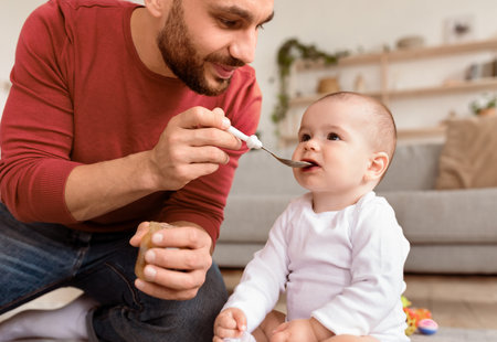 Loving Young Father Spoon Feeding His Little Baby Sitting Indoorsの写真素材