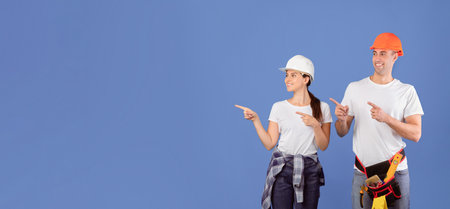 Cheerful Couple Of Workers In Hardhats Pointing Aside At Copy Space