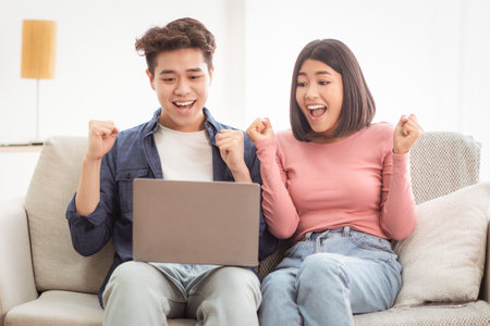 Joyful Chinese Boyfriend And Girlfriend At Laptop Shaking Fists Indoorの写真素材