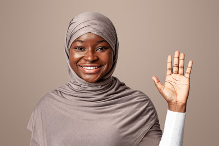 Hello Gesture. Friendly Black Muslim Lady In Headscarf Waving Hand At Cameraの写真素材